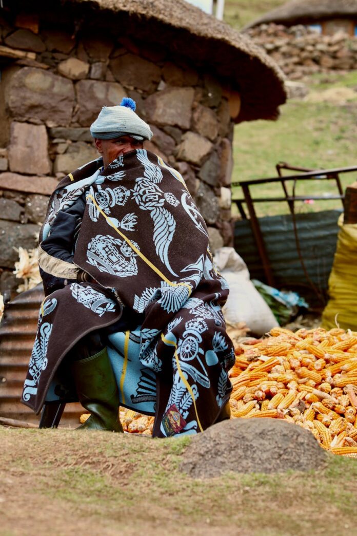 pexels-photo-10260794 man in traditional coat sitting by pile of corn